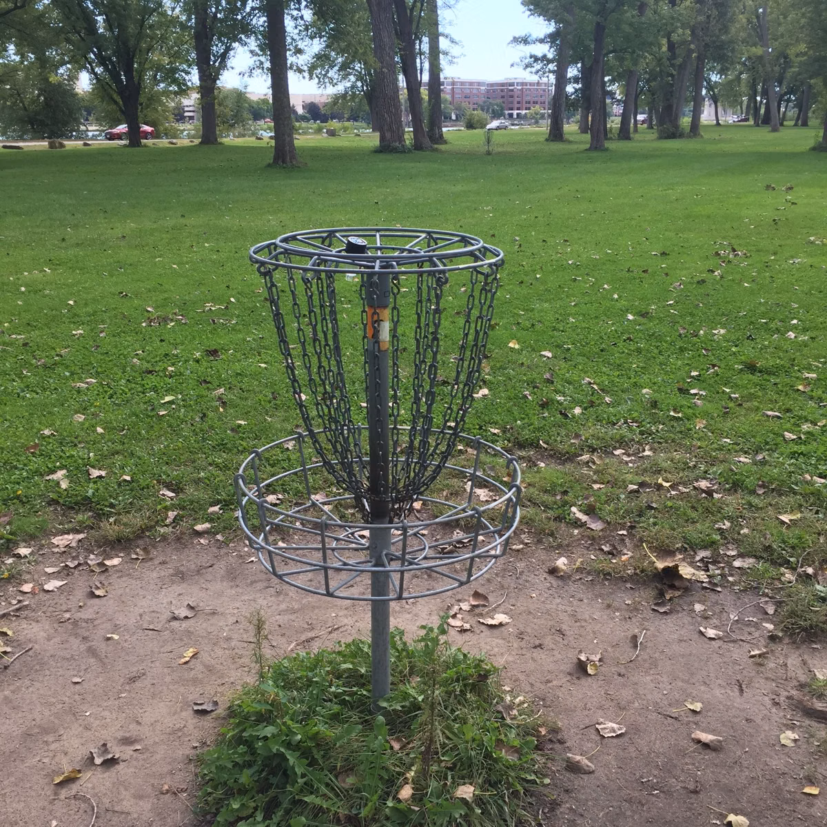 A metal disc golf basket on a grassy lawn with trees behind