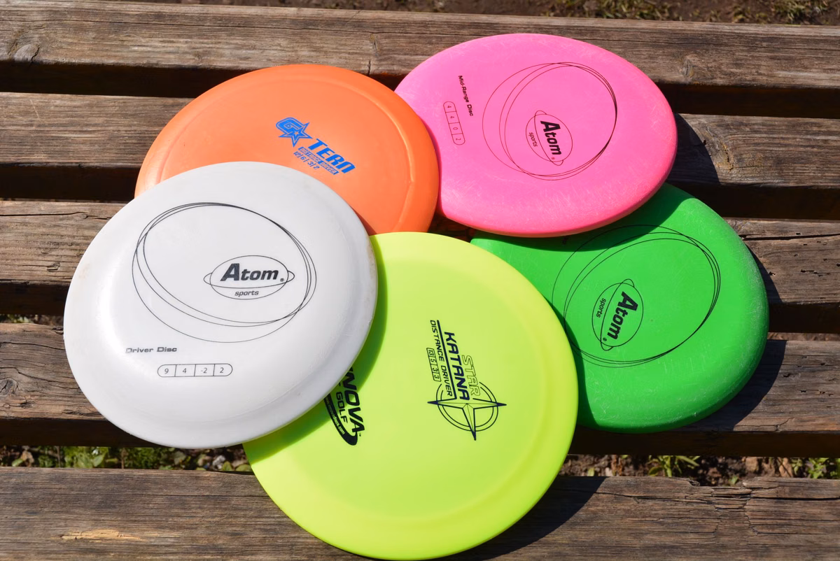 Four brightly colored disc golf discs on a wooden bench