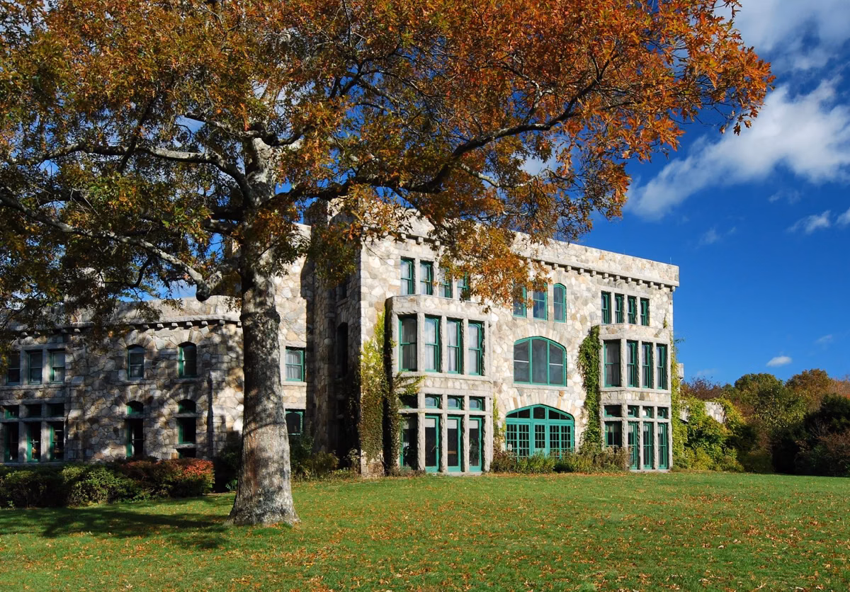 The stone Ames Mansion at Borderland State Park behind a large tree with autumn leaves, under a blue sky