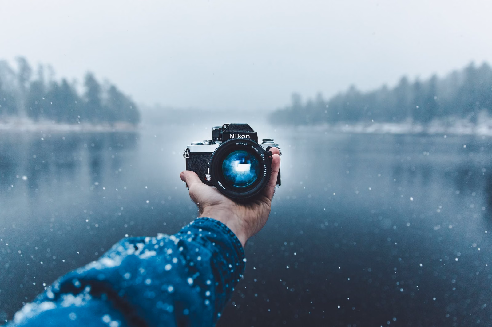A hand holding a camera in front of a snowy lake