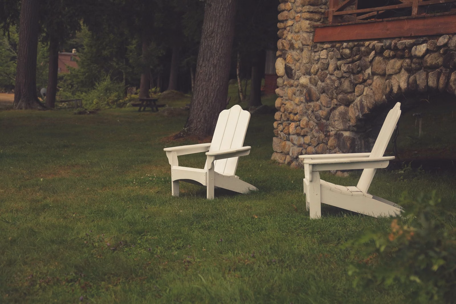 Two white lawn chairs on a lawn beside an old stone building